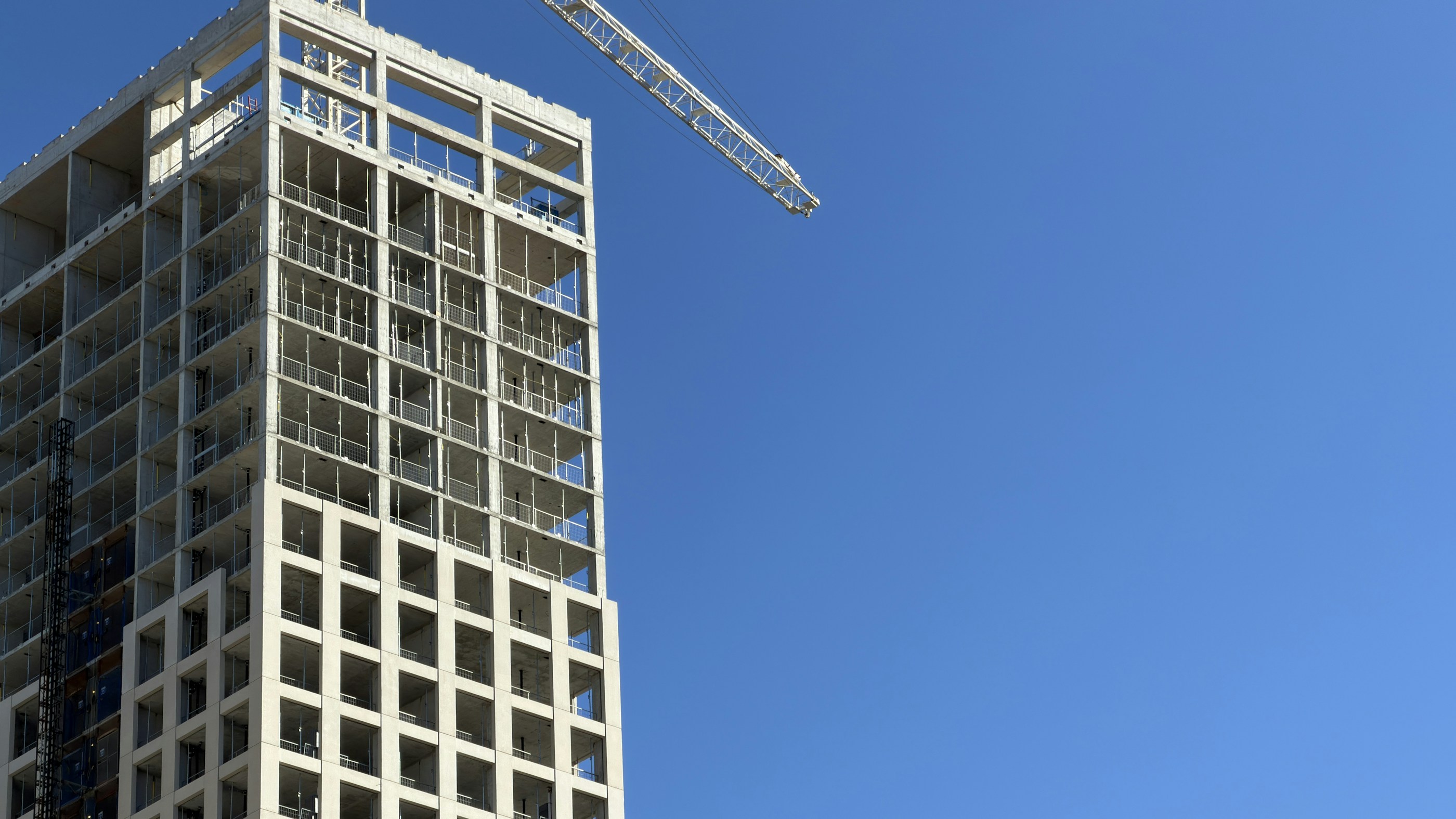 Struttura in cemento armato in costruzione e gru sotto un cielo azzurro